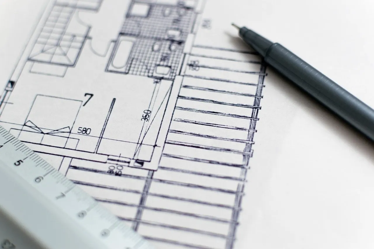 Architekturplan mit Grundriss, Maßangaben und Stift auf weißem Papier, daneben ein Lineal.