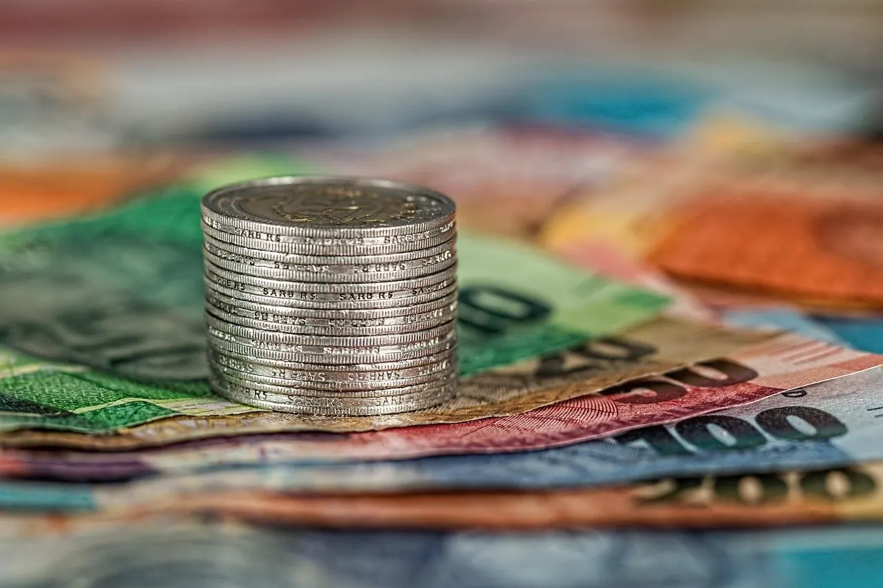 Gestapelte Münzen stehen auf mehreren unscharfen Geldscheinen mit Eurobanknoten im Hintergrund.