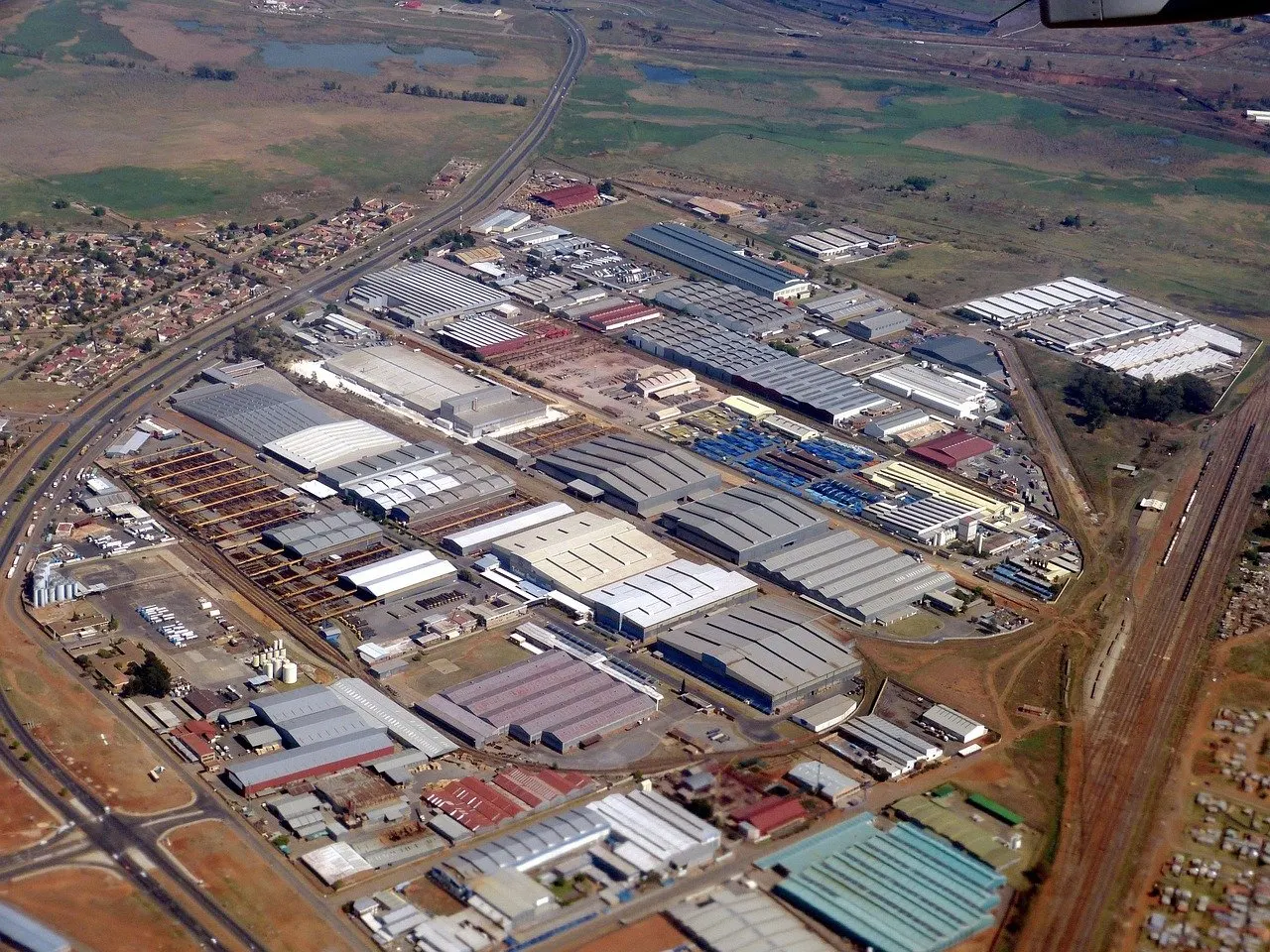 Luftaufnahme eines großen Industriegebiets mit Fabrikhallen, Lagerflächen, Bahngleisen und angrenzender Wohnbebauung.