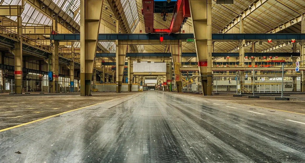 Leere, lange Industriehalle mit Stahlträgern, Laufkran und glänzendem Hallenboden.